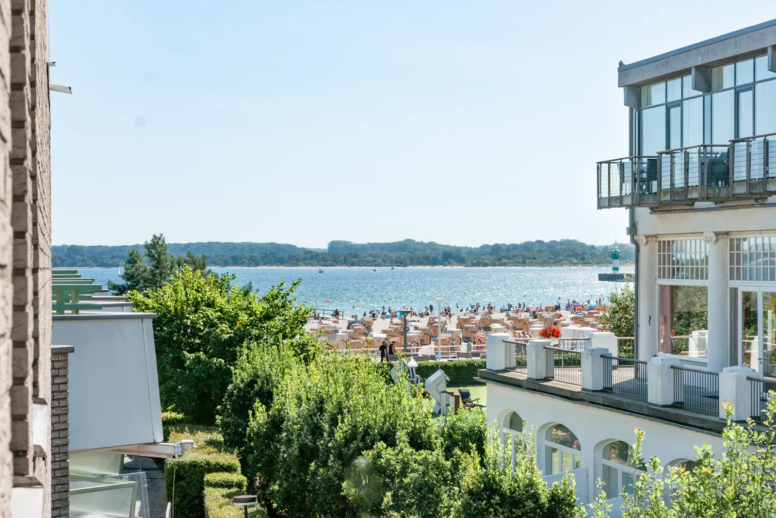 Blick vom Südbalkon über Bäume und Strandkörbe auf Kurstrand und Ostsee