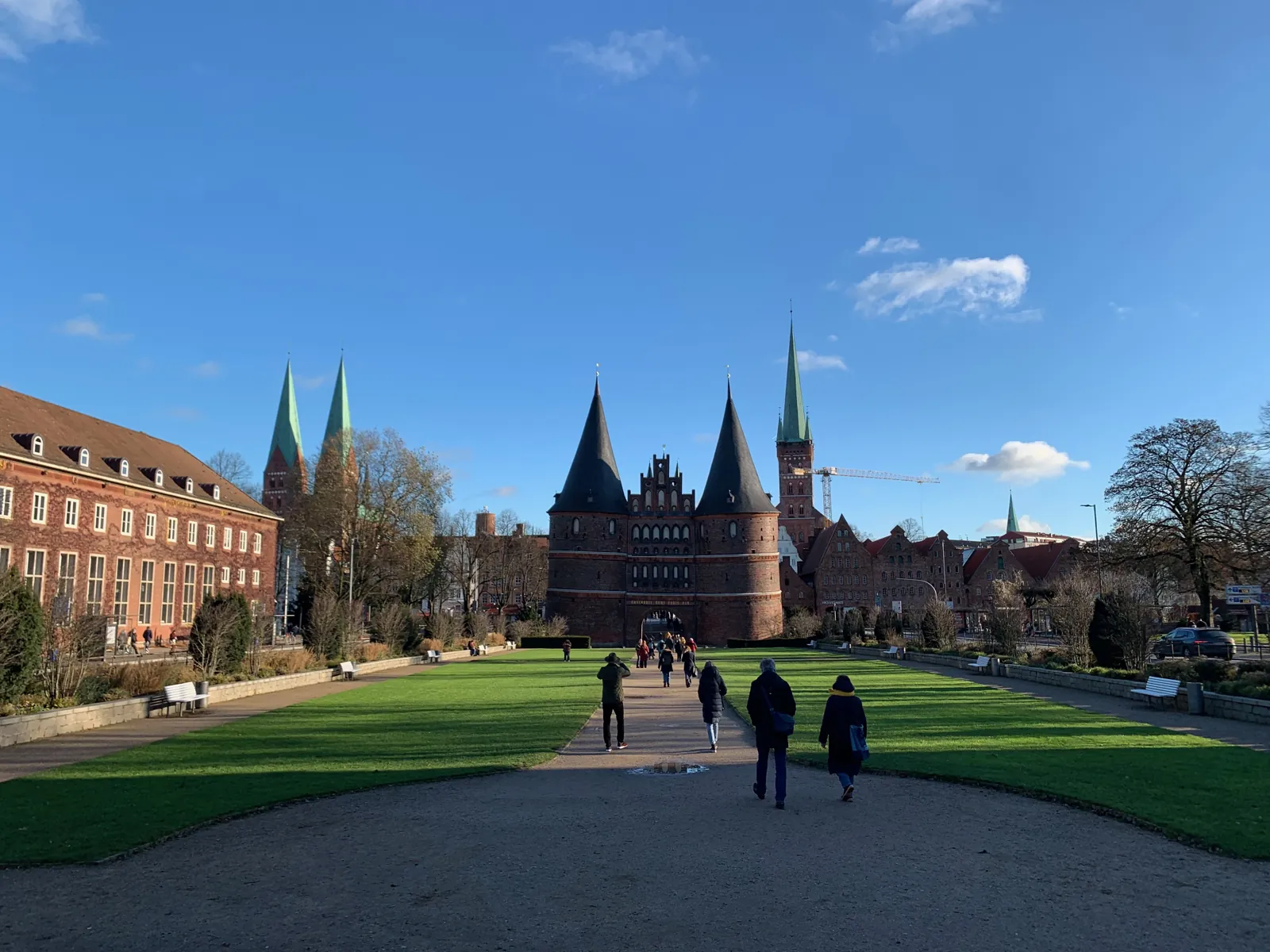 Holstentor in Lübeck im Spätherbst, davor eine Wiese mit Spaziergängern