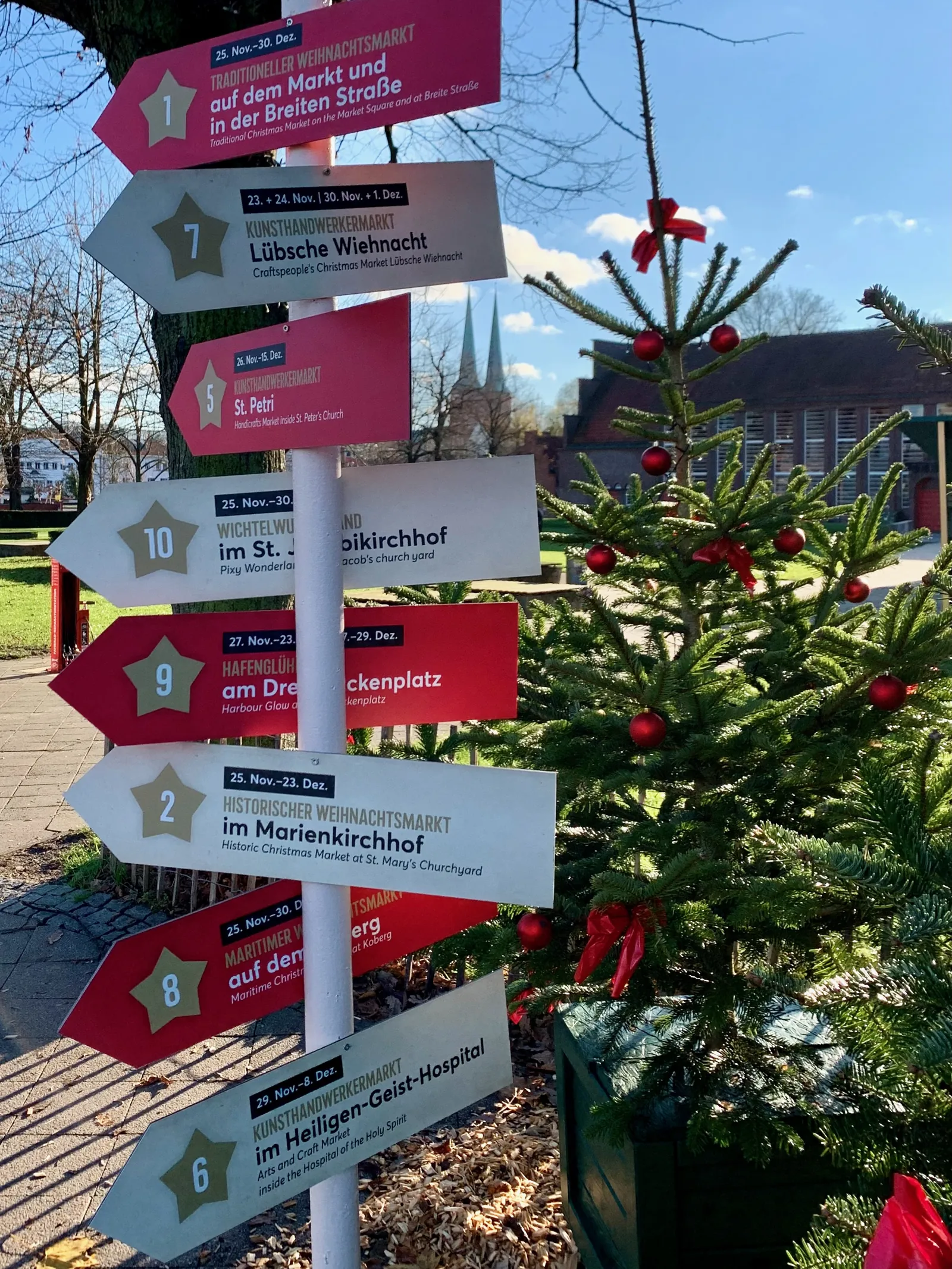 Wegweiser zu den Lübecker Weihnachtsmärkten neben einem geschmückten Tannenbaum