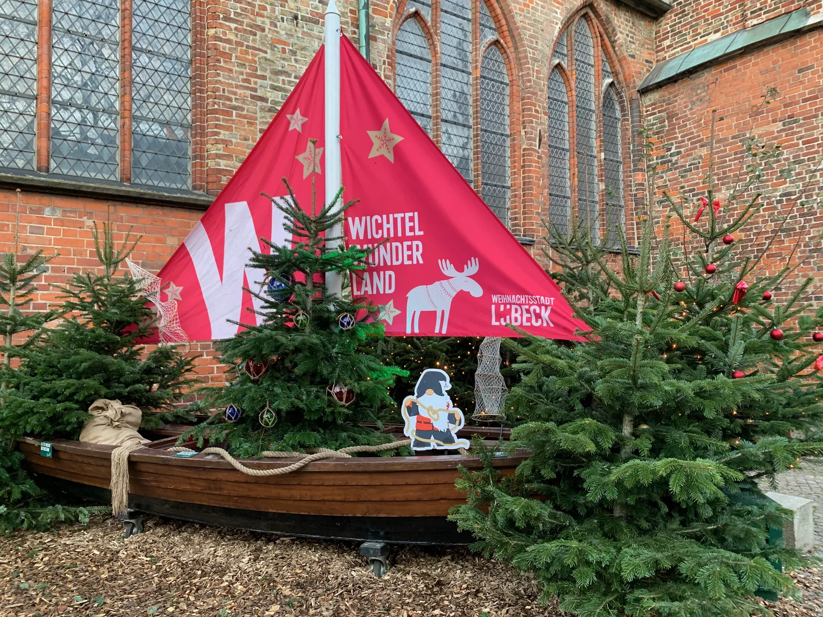 Eingang zum Wichtelwunderland an der Jakobikirche in Lübeck mit Tannenbäumen und Holzboot