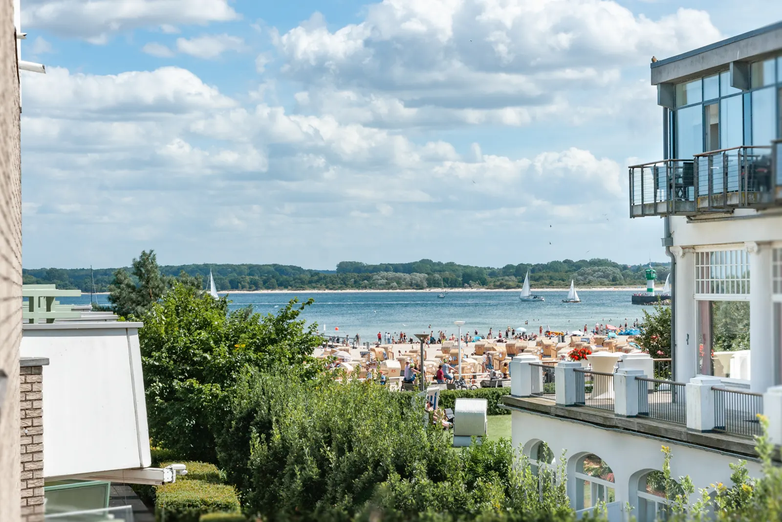 Blick vom Südbalkon über Bäume und Strandkörbe auf die Ostsee mit Segelbooten