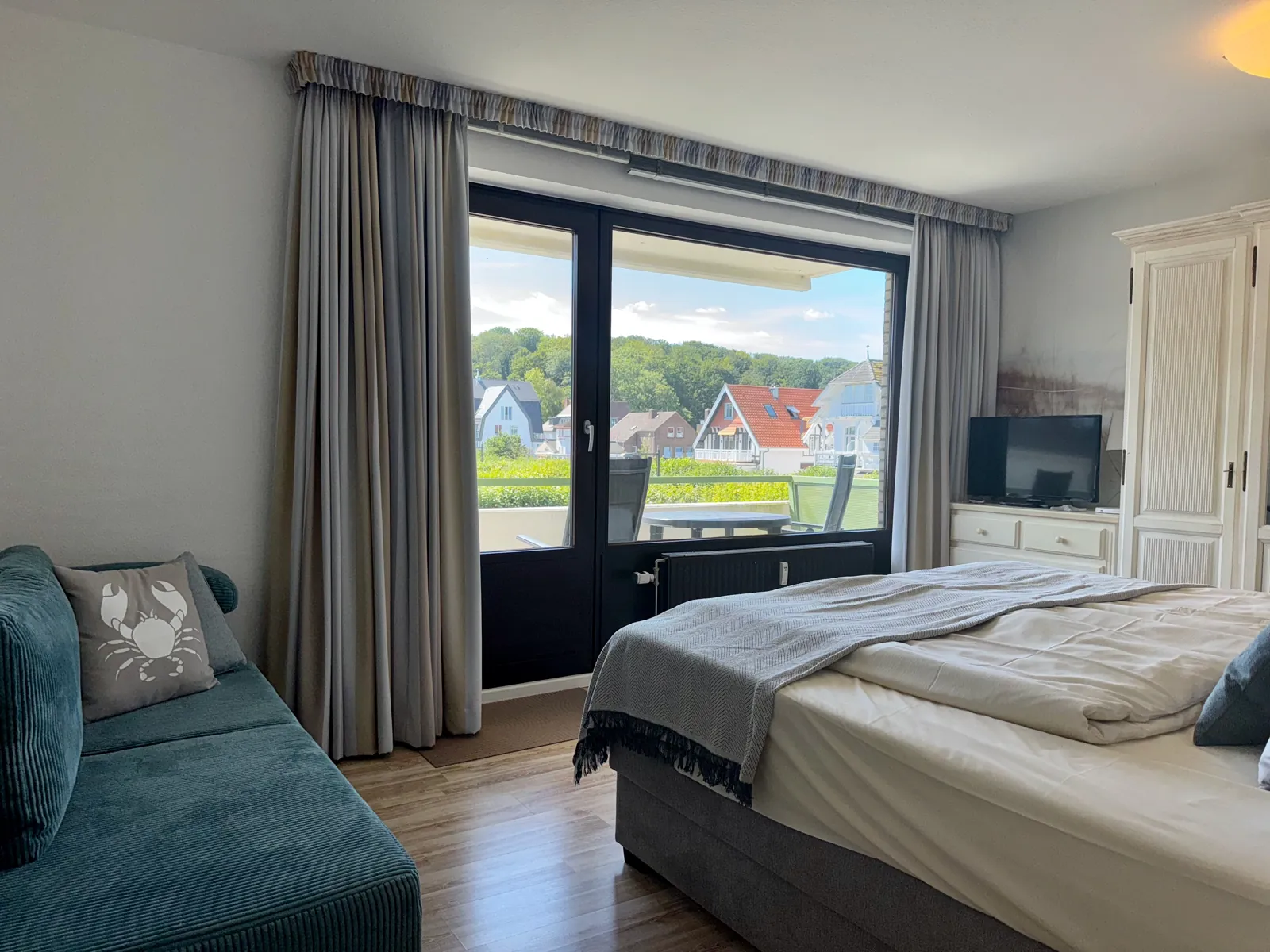 Schlafzimmer mit Boxspringbett, Schlafcouch, Fernseher und Tür zum Südbalkon