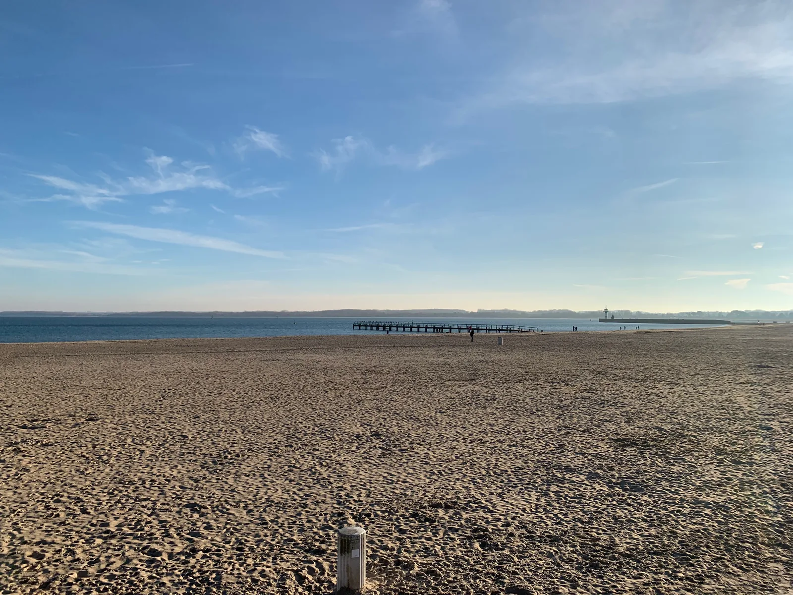 Leerer Sandstrand in Travemünde an einem klaren Wintertag, dahinter die ruhige Ostsee unter blauem Himmel