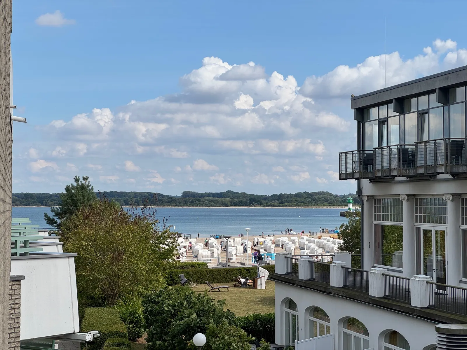 Blick vom Südbalkon der Ferienwohnung über Bäume und Strandkörbe auf Kurstrand und Ostsee