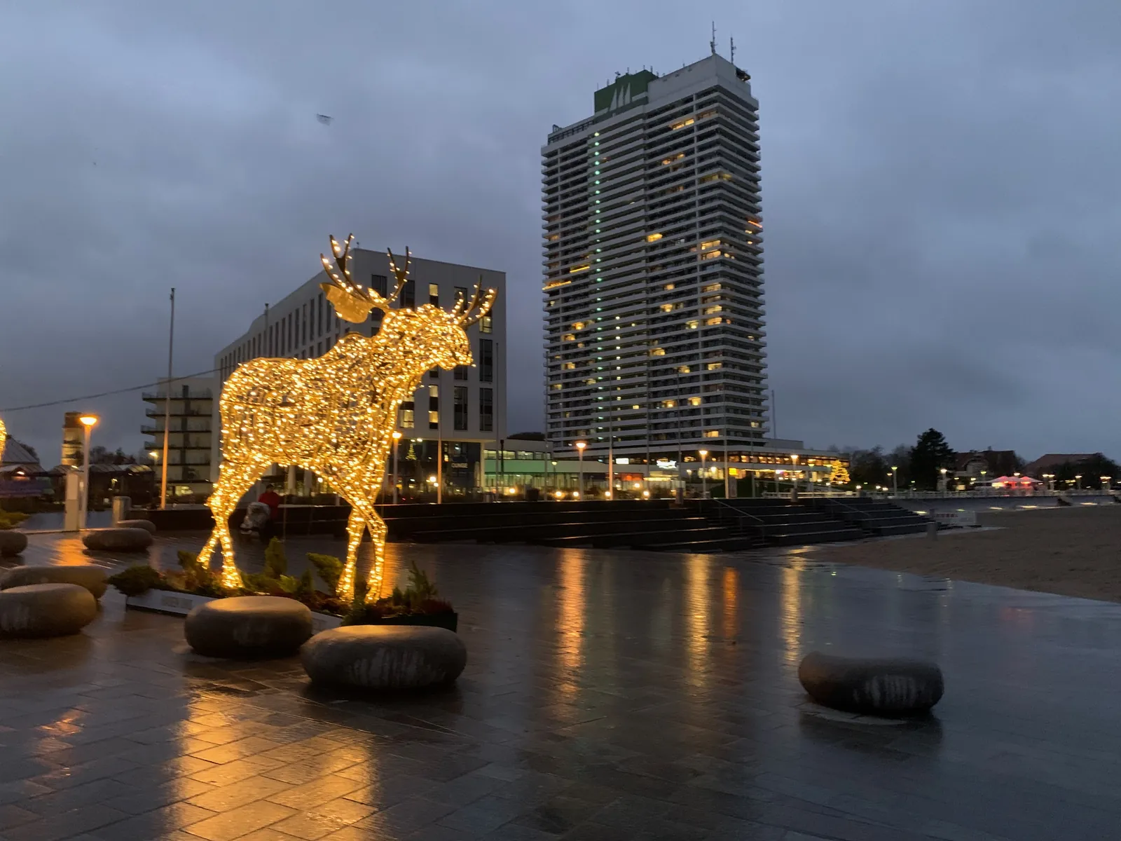 Ein leuchtender Elch an den Strandterrassen in Travemünde am Winterabend, dahinter das Maritim-Hochhaus