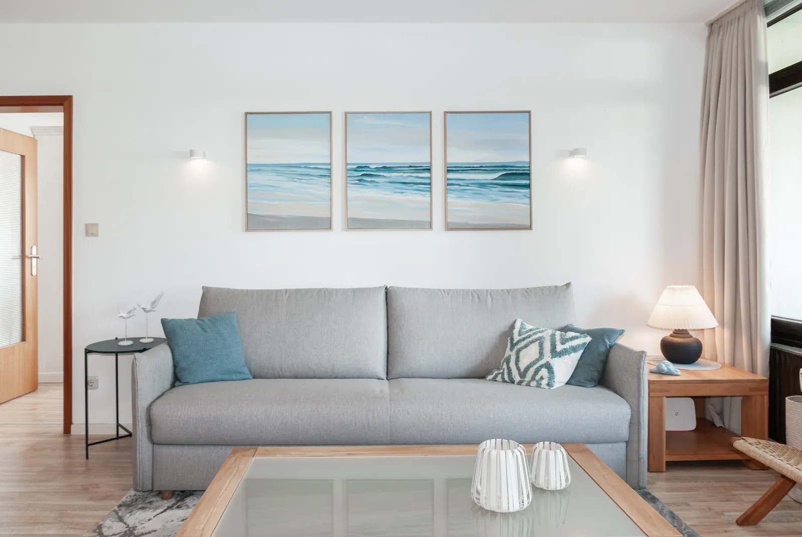 Wohnzimmer mit hellgrauem Sofa und drei Ostseebildern